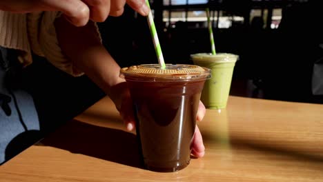 hand stirring coffee with green drink nearby