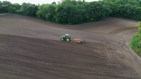 aerial tracking shot of a tractor plowing a field in the uk