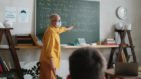 teacher in mask explaining formulas on chalkboard