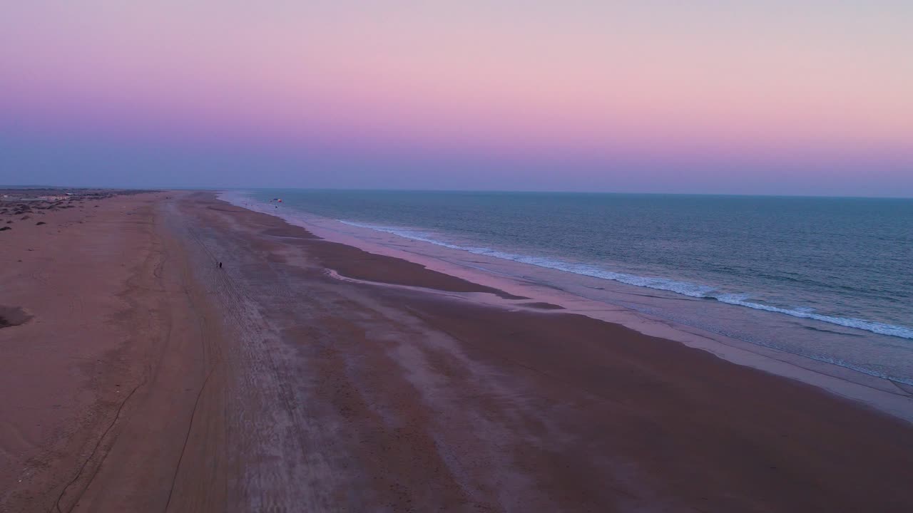 vasta playa con un cielo de puesta de sol púrpura con parapente alejándose