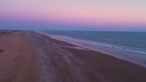 vast beach with a purple sunset sky with paraglider moving away