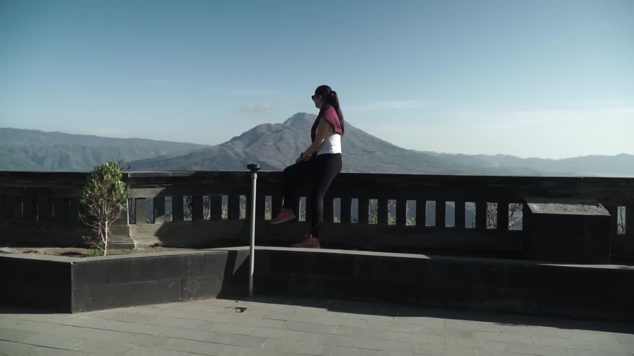 joven turista disfrutando de la vista de la mañana sentada en el borde y mirando a las montañas, cámara alrededor
