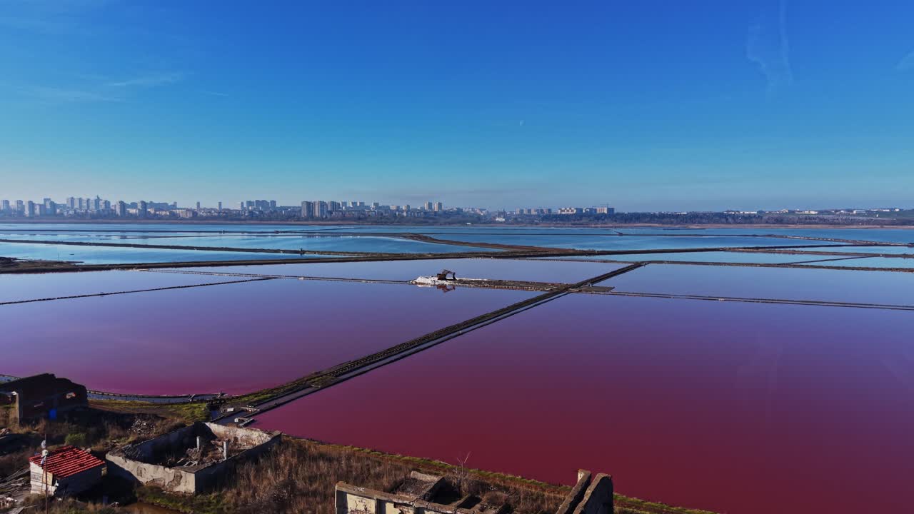 Salt pans in use near a city with water reflecting the sky