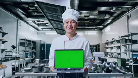 chef presentando una computadora portátil con pantalla verde en la cocina de un restaurante