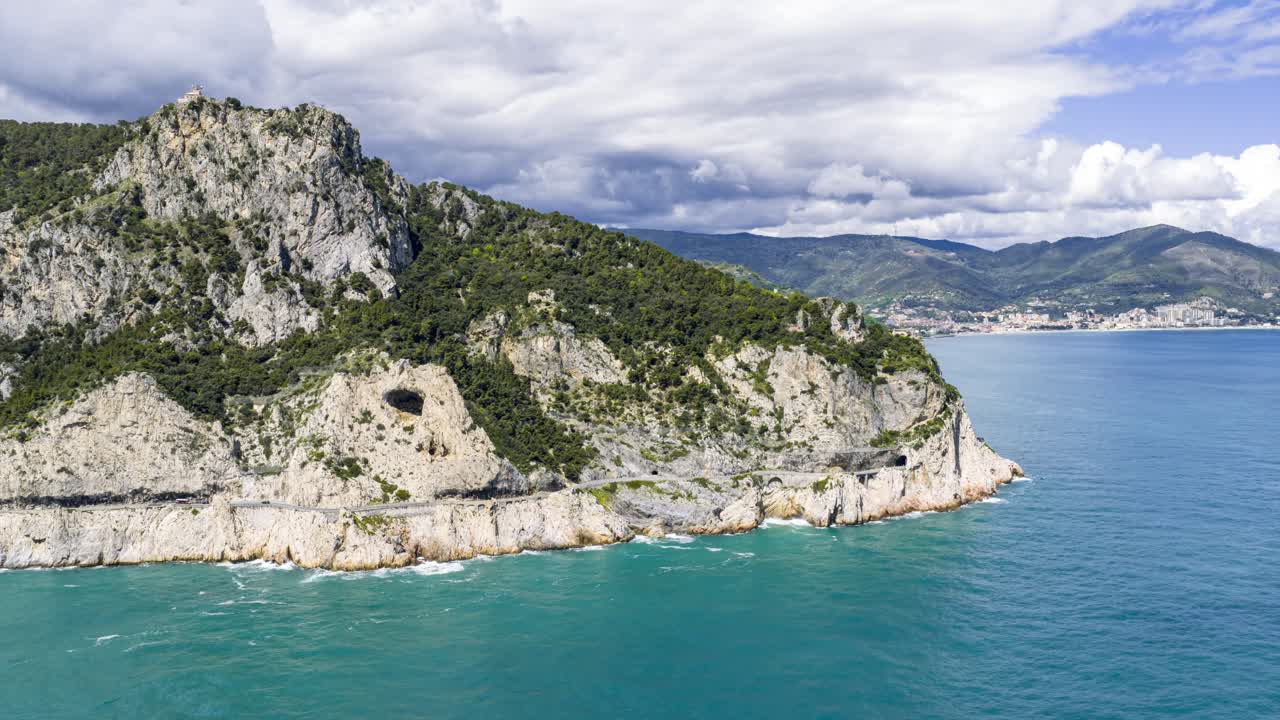 Noli, Italia, che mostra aspre scogliere che si ergono dal Mar Ligure turchese sotto un cielo nuvoloso.