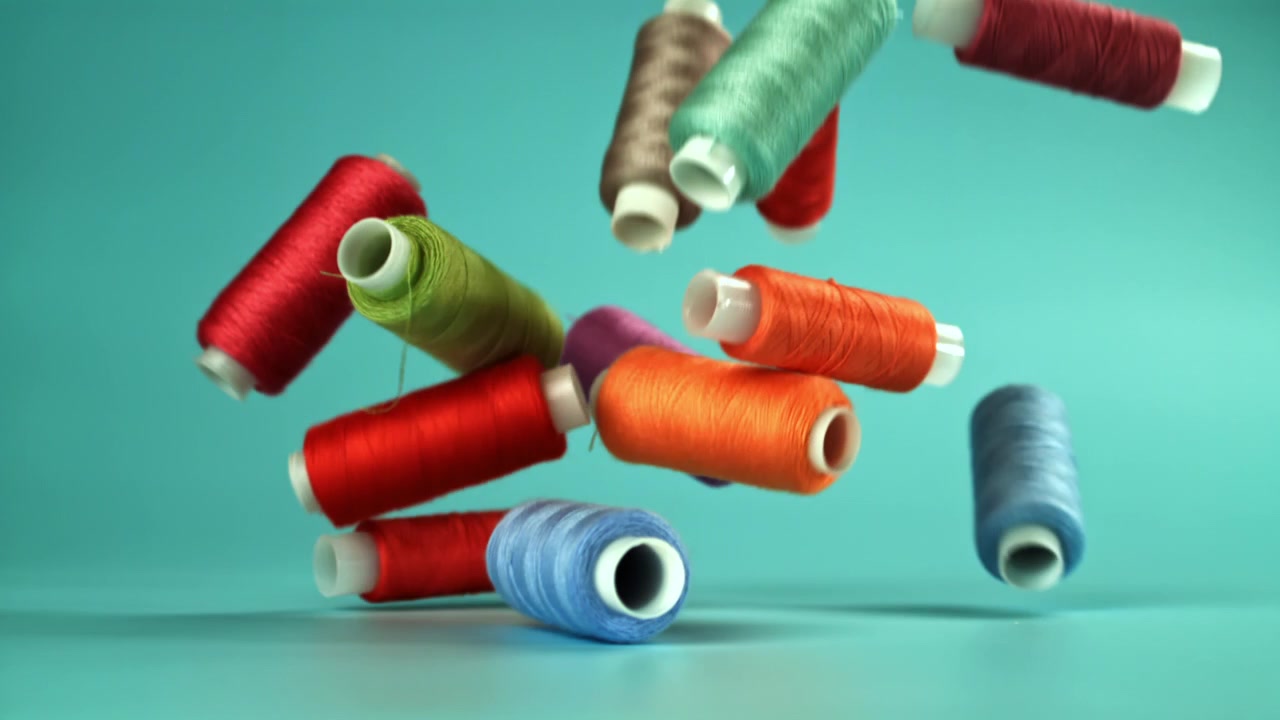 Colorful Thread Spools Falling in Slow Motion on Blue Background