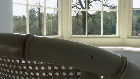 slow slide left over top of empty white wicker chair in window bay overlooking garden