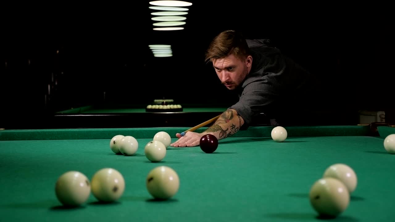 Een stoere man met tatoeages op zijn handen speelt Russisch biljart in een bar