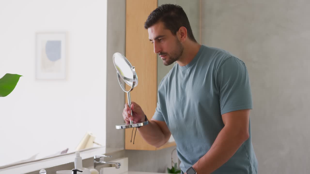 Hombre adulto inspeccionando su rostro en el lavabo del baño con un espejo de aumento, revisando la piel después de asearse.