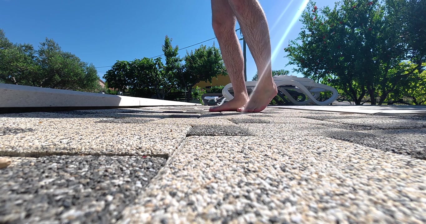 bare feet walking on a sun-heated pool deck beside a swimming pool. Ideal for concepts of hot weather, summer heat, outdoor leisure, vacation, poolside lifestyle, and seasonal temperatures.
