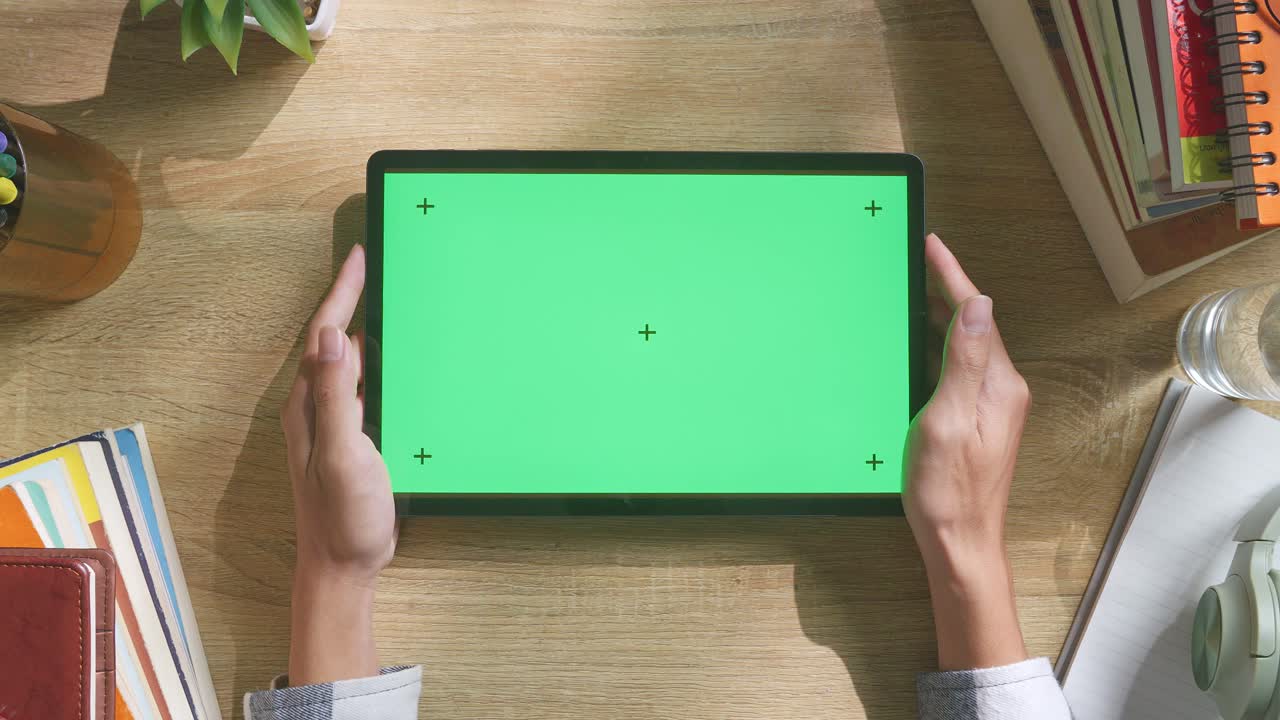 초록색 화면을 모방한 노트북 컴퓨터의 상단에서 아래로 볼 때, 펜, 안경, 그리고 물 한 잔을 가진 노트북 에 나무 사무실 책상 위에 크로마키 디스플레이가 있습니다.