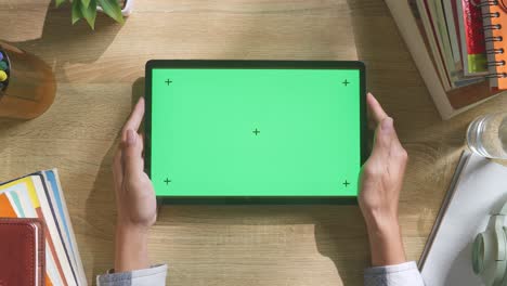 vista de arriba hacia abajo de una computadora portátil con pantalla verde simulada pantalla chromakey en un escritorio de oficina de madera al lado de la libreta con bolígrafos, gafas y un vaso de agua.