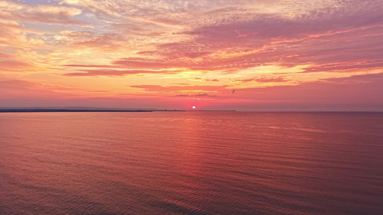 Solnedgang over roligt vand med orange og lyserød himmel i aftentimerne