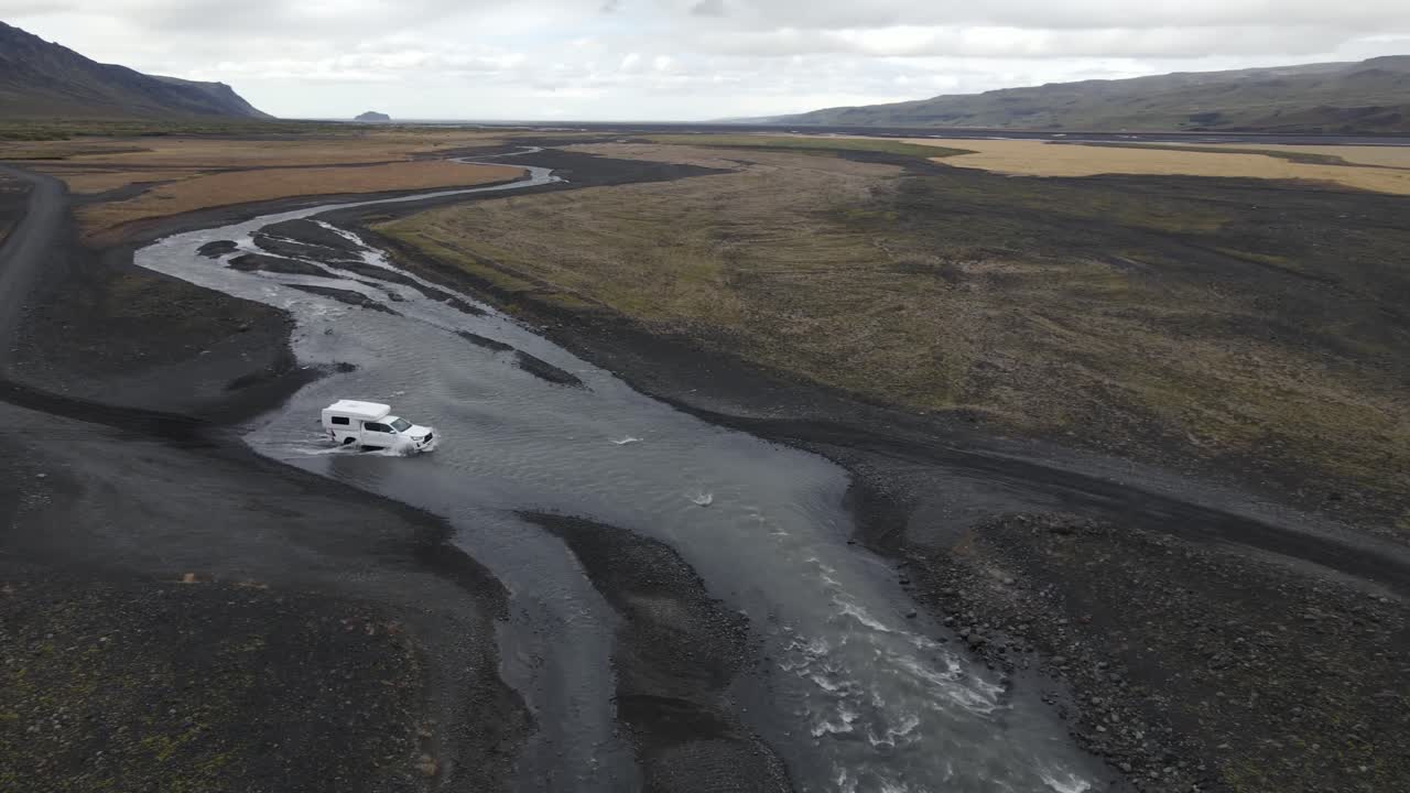 Vista aerea con drone che riprende veicoli che attraversano un tortuoso fiume vulcanico con terreno di ghiaia scura e canali d'acqua che scorrono in un paesaggio remoto dell'Islanda.