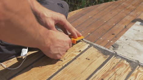utilizando un raspador eliminando la masilla residual de los tablones del techo del barco