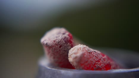 Two hot shisha charcoals glow red, covered in ashes, burning inside a metal narguile container