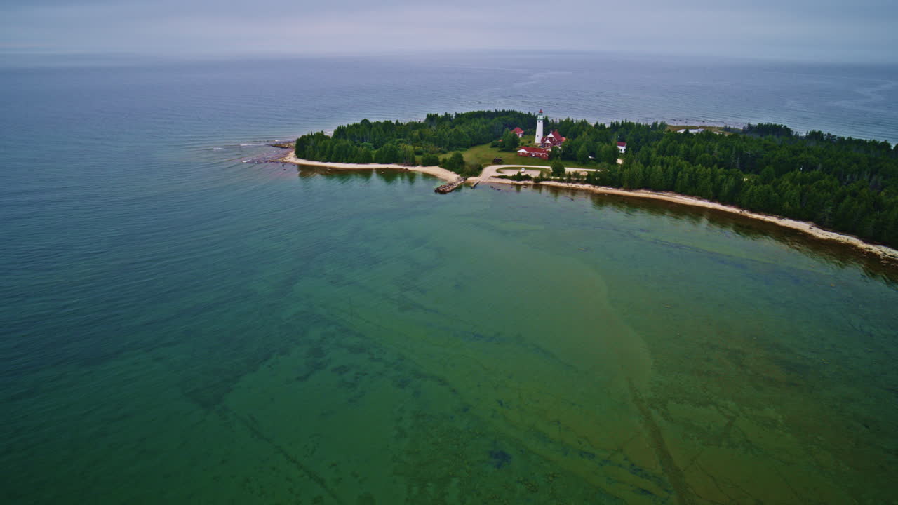Drone shot flying over interesting rock formation in Lake Michigan towards a lighthouse that sits on the point