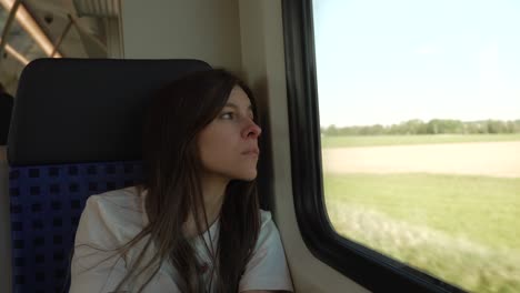 young brunette woman looking at train window, green countryside rural field