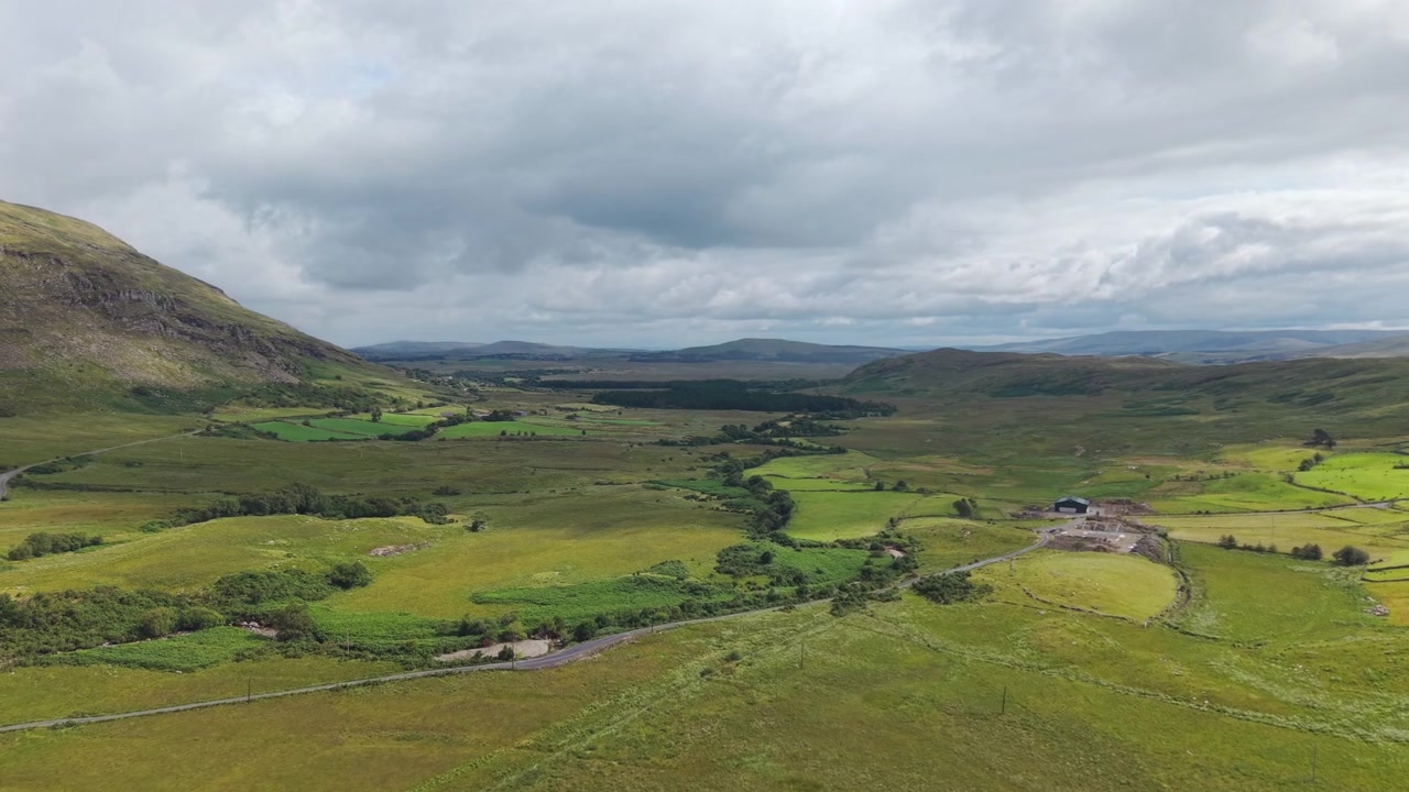 Un'ampia ripresa aerea della vibrante campagna verde e delle dolci colline della Contea di Mayo, Irlanda, sotto un cielo nuvoloso e drammatico. Perfetto per temi di viaggio e sostenibilità