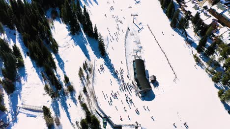 aerial drone view of busy ski slope with people riding cairlift, reveal of tall mountain peak with crowded trails