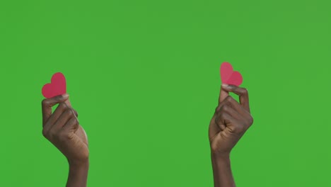 manos sosteniendo corazones de papel en la pantalla verde