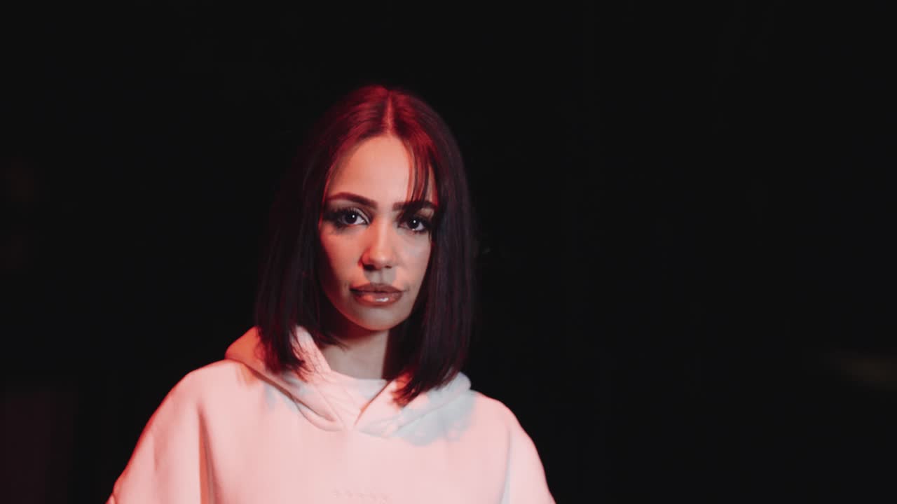 Young beautiful woman with white sweater. in the night looking into the camera, dark environment