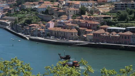 scenic douro river landscape and lined-up residential buildings with traditional wooden boats navigating the calm waters in portugal