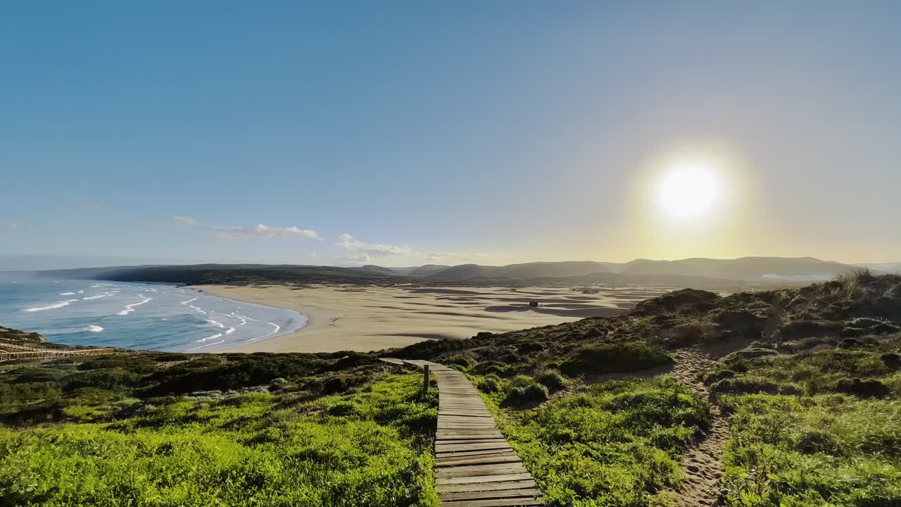 golden hour over sandy beach and ocean waves in portugal seen from grassy trail