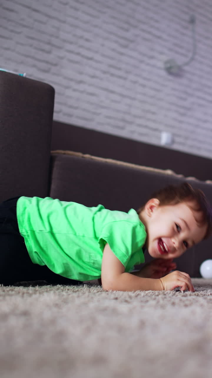 Playful little kid rolling on the floor in the room. Happy smiling boy crawls up to a camera. Vertical video