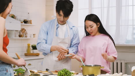 two japanese women and man are cooking japanese food while talking and laughing in the kitchen