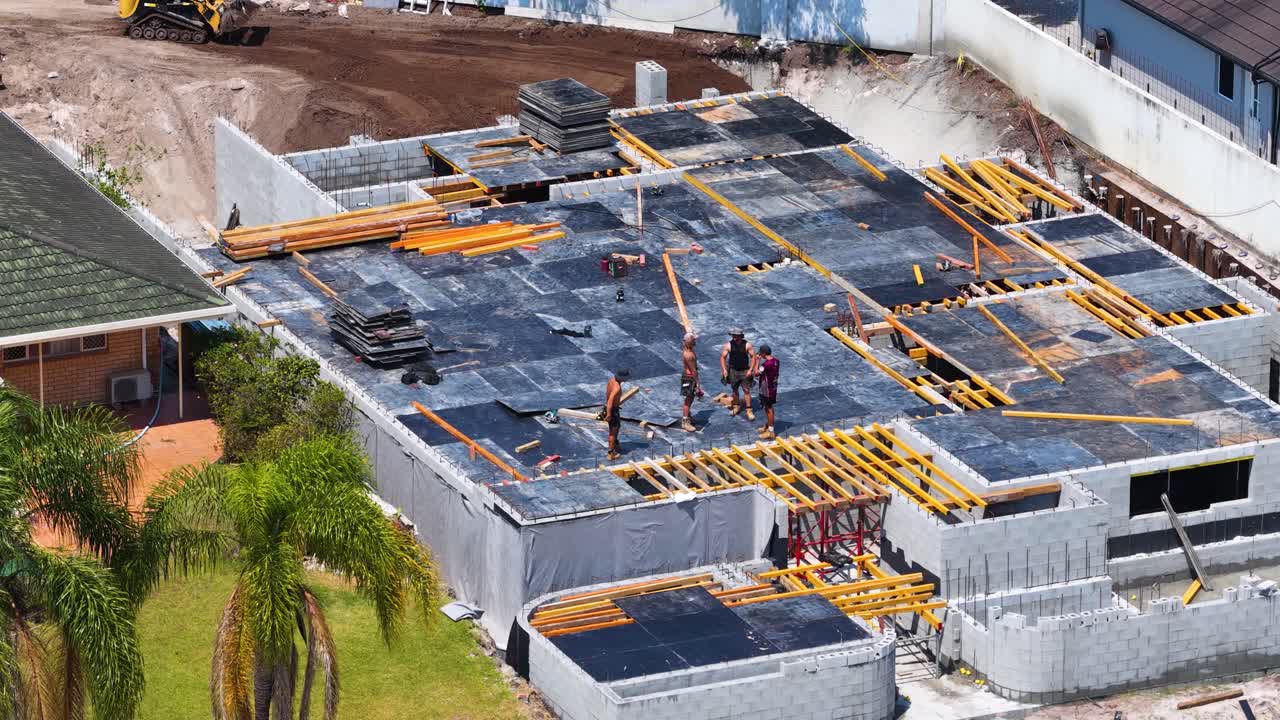 Aerial daytime shot of construction workers arranging timber formwork on residential concrete slab foundation