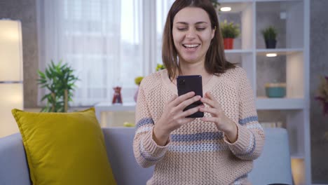 una adolescente feliz usando un dispositivo de teléfono inteligente en casa.