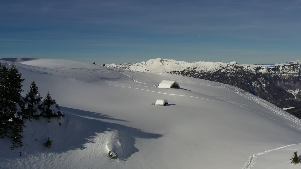 vista aérea volando hacia una cabaña de montaña cubierta de nieve en los alpes franceses en invierno, antes de volar sobre el borde de la colina y revelar el valle y las montañas