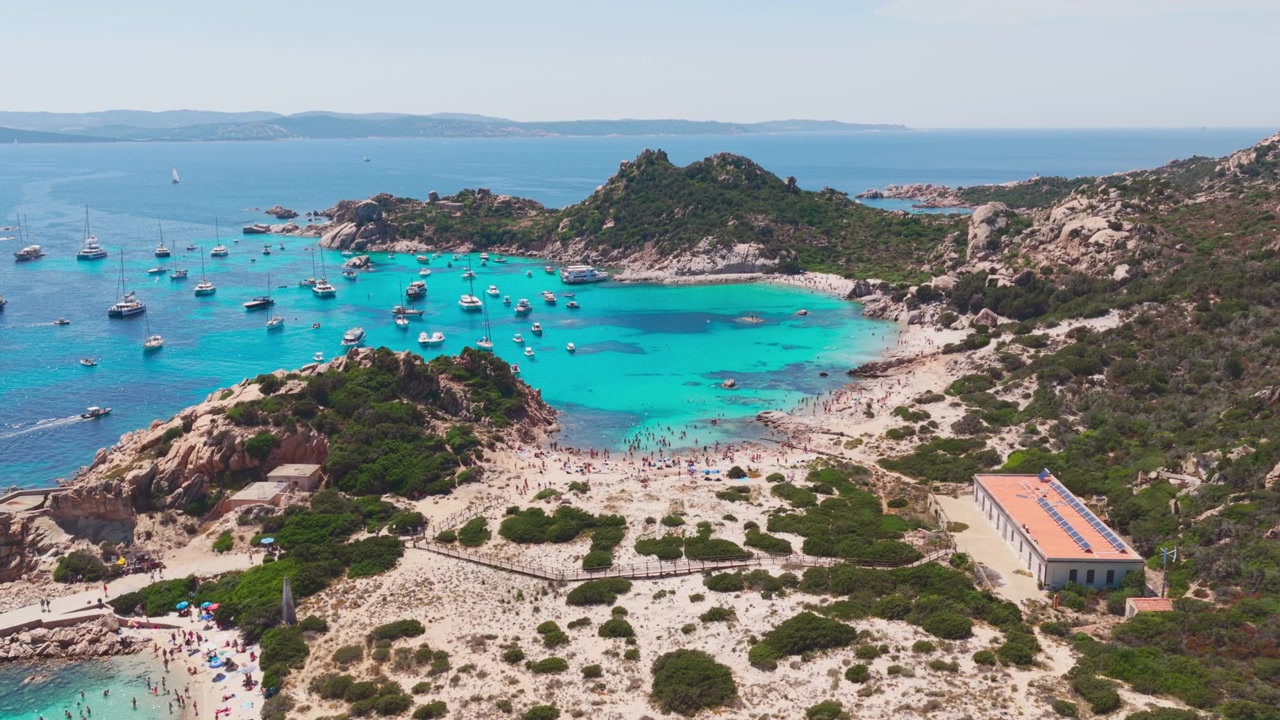 Large vue aérienne survolant des yachts de luxe dans des eaux bleu turquoise, avec une magnifique plage de sable nichée dans des falaises de granit sur l'Isola di Spargi dans l'archipel de la Maddalena en Sardaigne, Italie