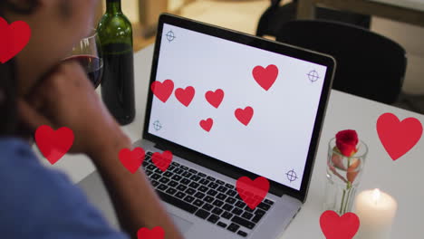 animation of hearts over biracial man drinking wine and using laptop with copy space
