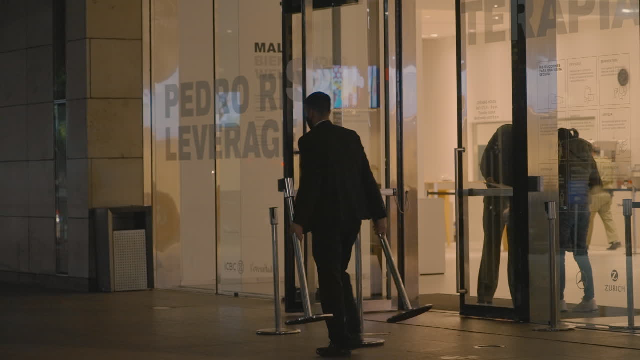 Uomo che sistema paletti all'esterno dell'ingresso di un moderno edificio di vetro.