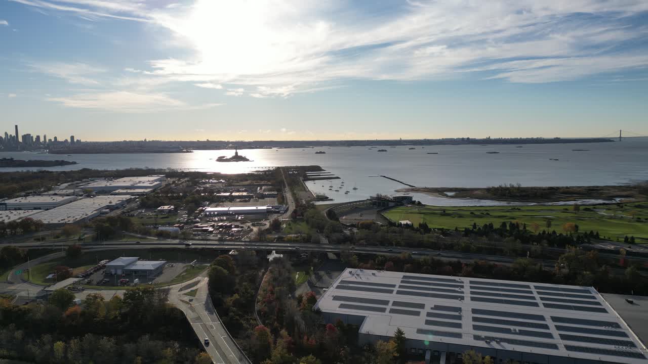 A smooth aerial flight over Jersey City moves directly toward Manhattan, revealing dense streets, layered highways, and the full New York City skyline