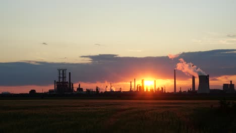 Brilliantly-Red-Orange-Sunset-over-Oil-Refinery,-Wheat-Field-Foreground,-4K