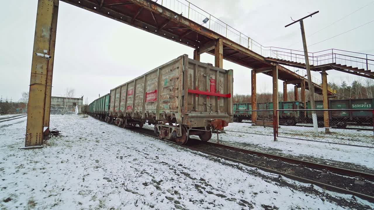 United containers with cargo are moving on rails at the railway station under the bridge on a winter day. Logistics.