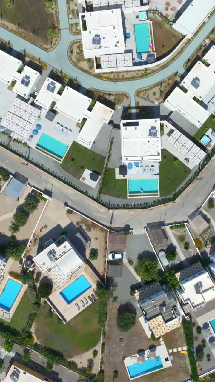 Vertical drone shot over holiday homes with pools on top of a hill in Greece