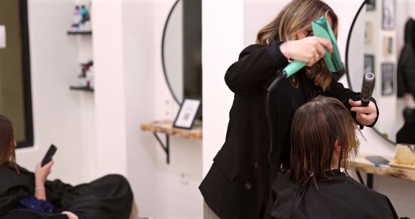 Professioneller Friseur trocknet Haare einer Kundin im Salon
