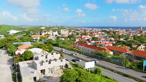 Drone-rises-above-tropical-brush-to-reveal-Willemstad-as-cars-race-by-on-highway-with-ocean-views