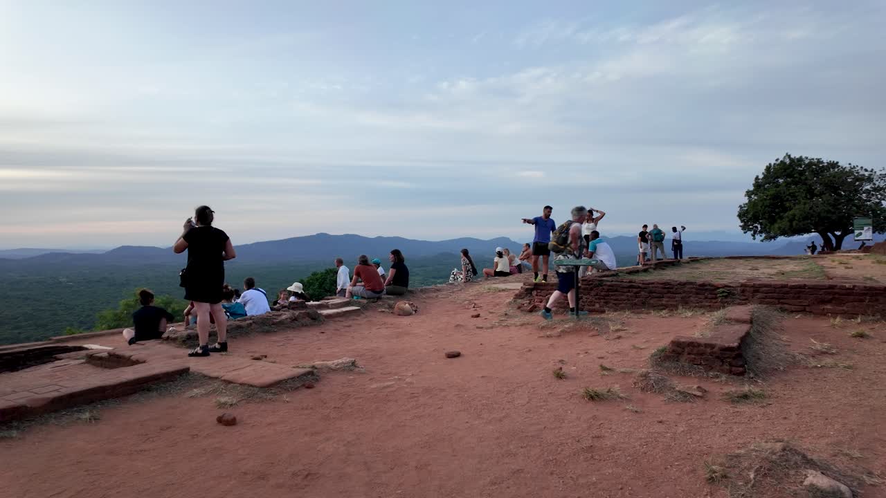 Visitors gather on an ancient plateau, with ruins and panoramic views, enjoying the serene atmosphere of archaeological significance and natural beauty surrounding them.