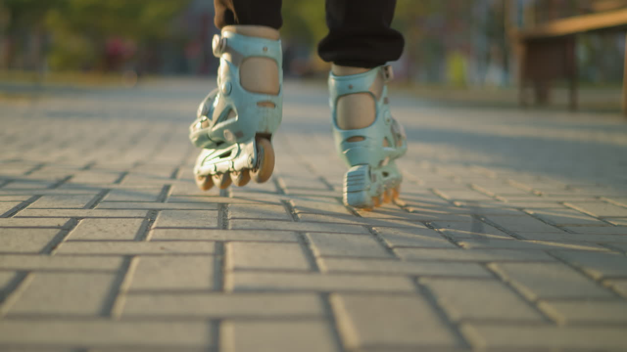 A back shot focusing on a person s feet wearing rollerblades as they glide smoothly along a paved path in a park. The background is softly blurred, drawing attention to the motion of the rollerblades