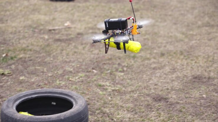 Drone che vola basso su un campo sterrato mostrando movimento controllato e sistema di carico utile in funzione