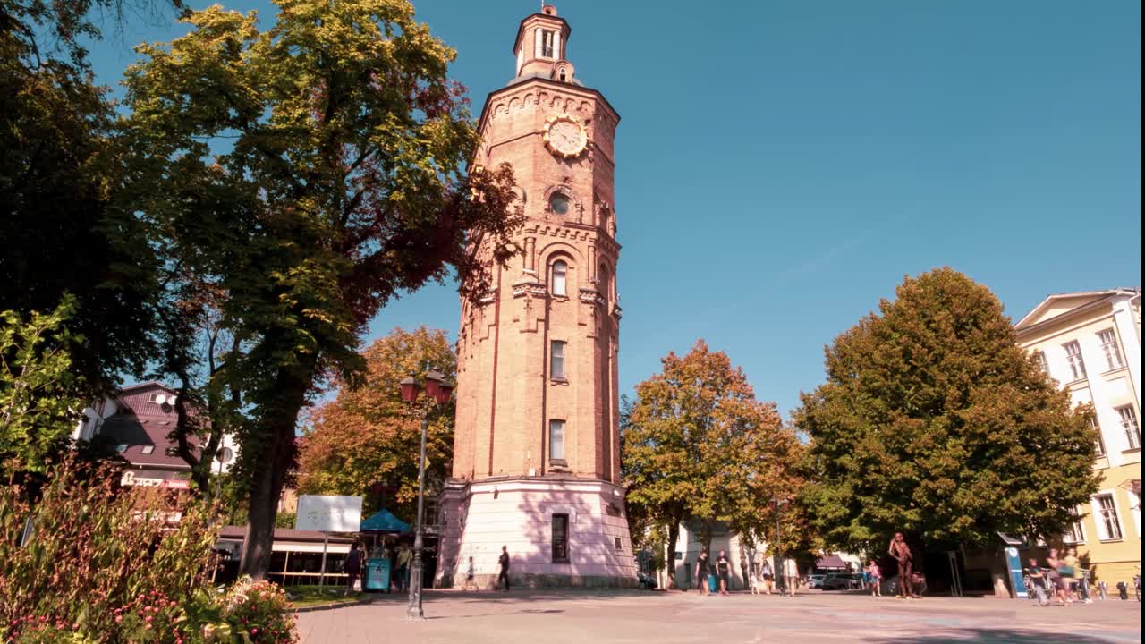 Timelapse video of people walking in a beautiful park with many trees and a clock tower