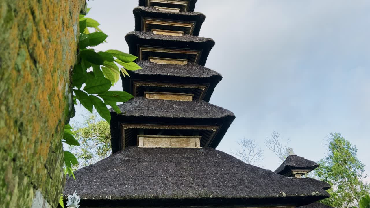 Lavvinkelperspektiv af et traditionelt balinesisk Meru-tårn med lagdelte stråtag, der rejser sig mod en klar blå himmel og viser klassisk tempelarkitektur på Bali, Indonesien.