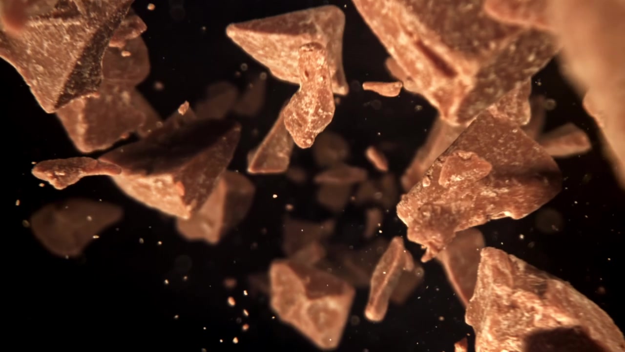Pedaços de chocolate caindo em câmera lenta sobre fundo preto.