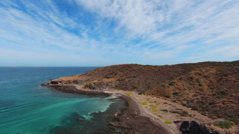 aerial view along wild seashore and brown hill overlooking turquoise ocean in region of baja mexico, wilderness landscape