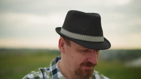 a man in a black hat and a checkered shirt is intensely focused on an unseen task, with mosquitoes visibly flying around his head. his deep concentration creates a serene yet determined atmosphere